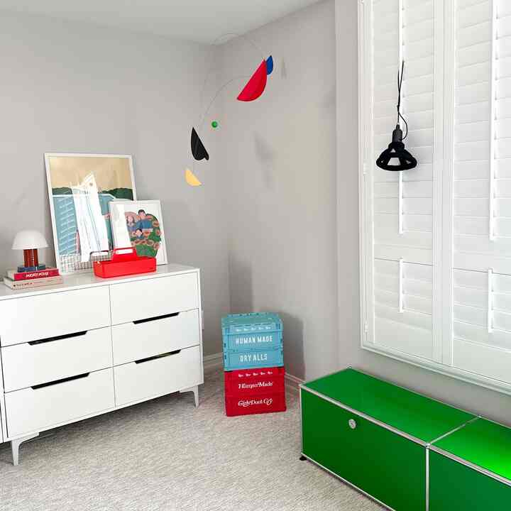 White-toned kids' room featuring clean storage furniture, green USM storage units, and a playful mobile, creating a modern atmosphere
