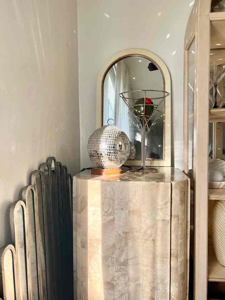 Beige marble console corner featuring a silver disco ball and martini glass, sparkling under afternoon sunlight