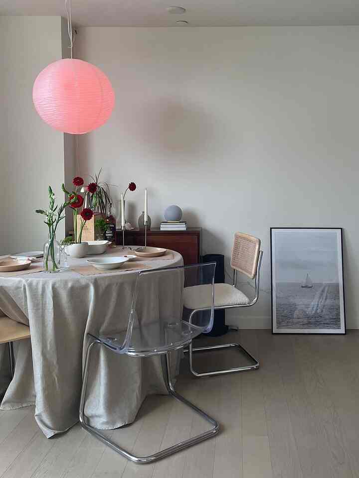 Natural wood tone flooring and white walls dining room, round dining table with tablecloth, transparent and rattan chairs create cozy atmosphere