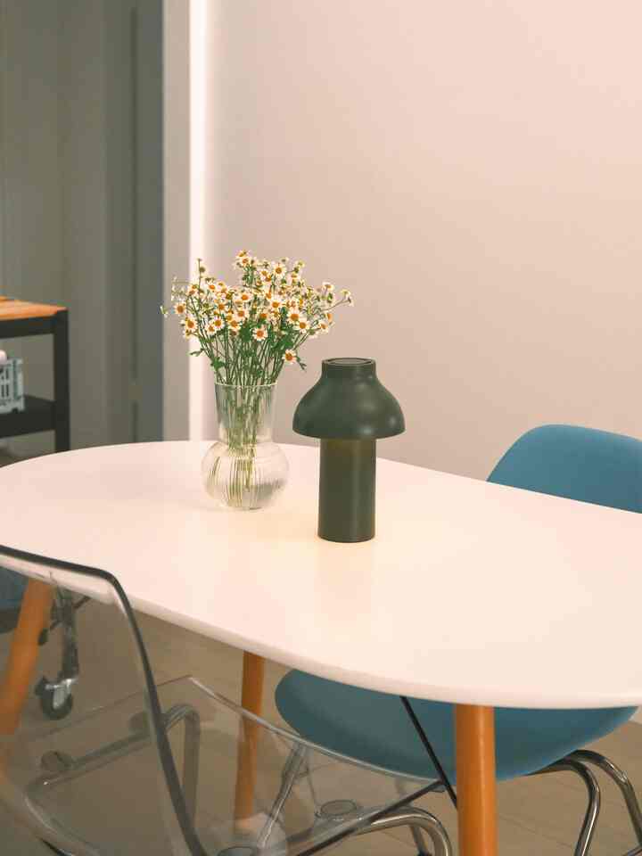 Bright natural-toned dining room featuring a white table with wood legs, glass vase with flowers, and table lamp creating a clean atmosphere