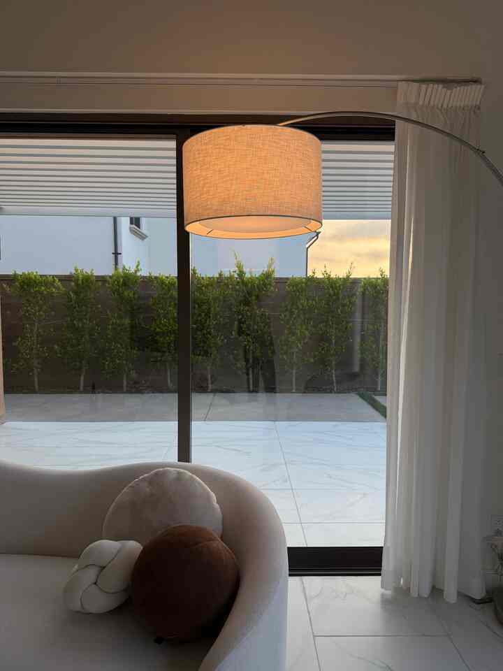 Warm beige and white-toned living room featuring a curved corner sofa and stylish floor lamp in a minimal interior space