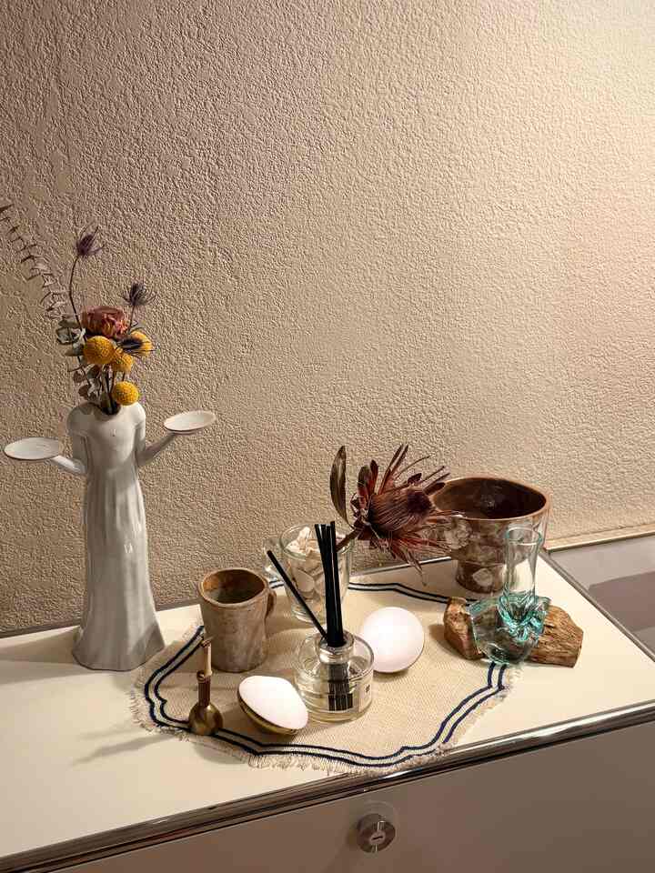 A cozy corner space with beige textured walls and a cream sideboard topped with various natural material objets and a diffuser