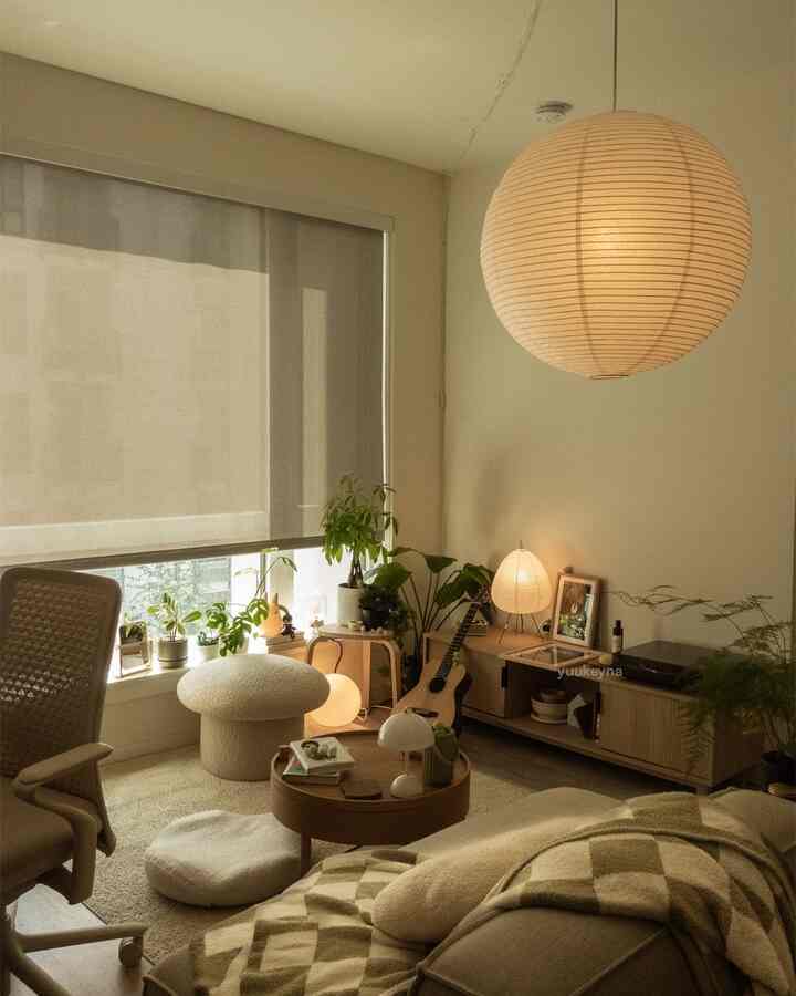 Natural wood tone and beige living room featuring round coffee table, stool, and various plants creating a cozy atmosphere