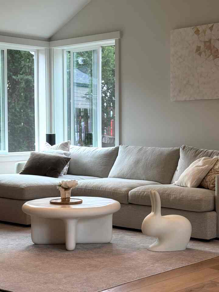 Soft ivory and gray toned living room with a large sectional sofa, round coffee table, and a playful rabbit-shaped chair creating a warm, cozy atmosphere