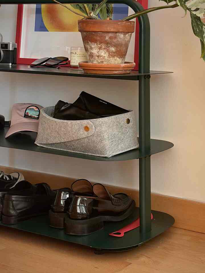 Dark green shoe cabinet with a gray felt basket and terracotta pot on the middle shelf in a residential entrance interior