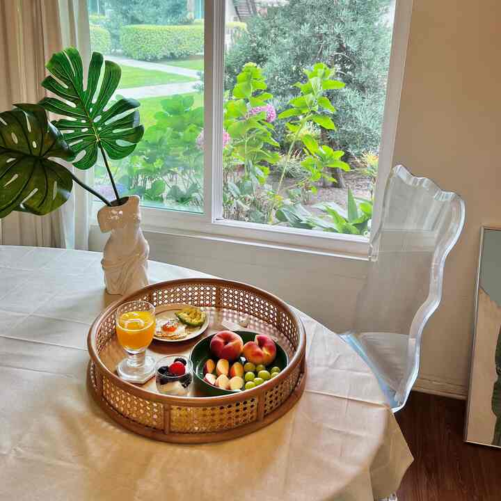 Beige linen tablecloth and rattan tray on a natural modern dining table by a window seat, cozy home party space with natural light