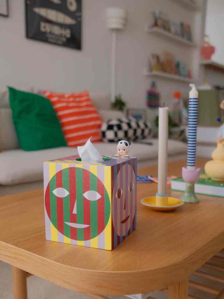 A white and natural wood tone living room featuring colorful striped cushions and patterned candles on a cozy coffee table