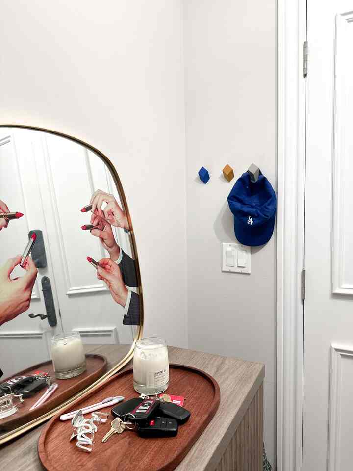 Entrance area with white walls and wood tone cabinet, gold framed mirror and a tray holding candle and keys, neat and stylish