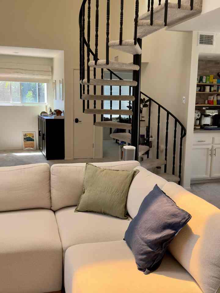 Beige-toned living room featuring a black spiral staircase and sectional sofa creating a cozy atmosphere