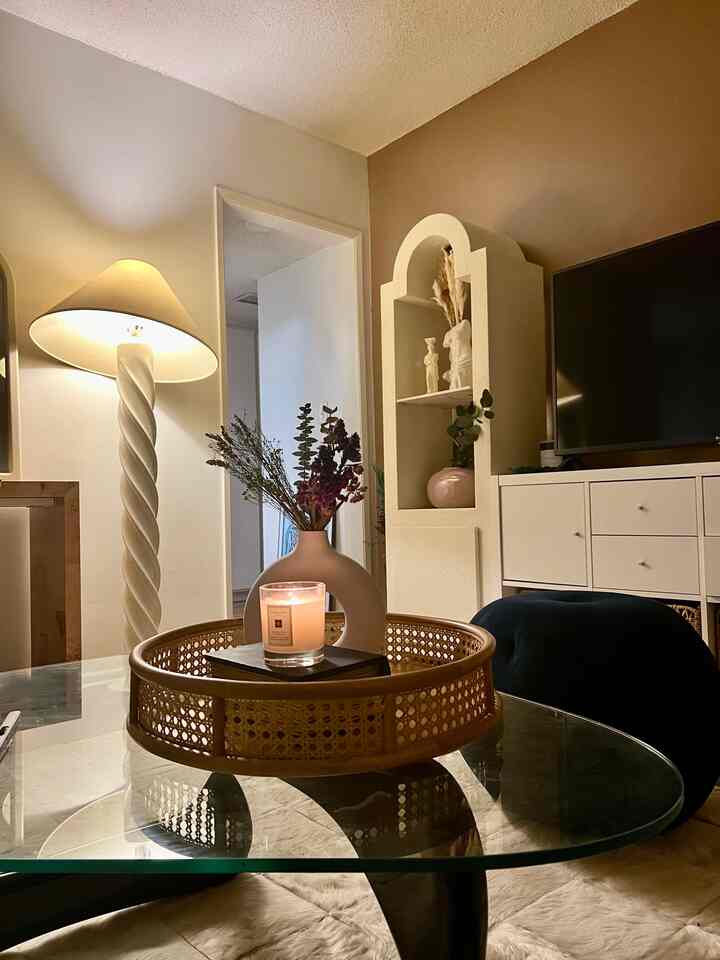 Beige and white toned living room featuring glass coffee table with rattan tray and lit candle, creating a cozy ambiance