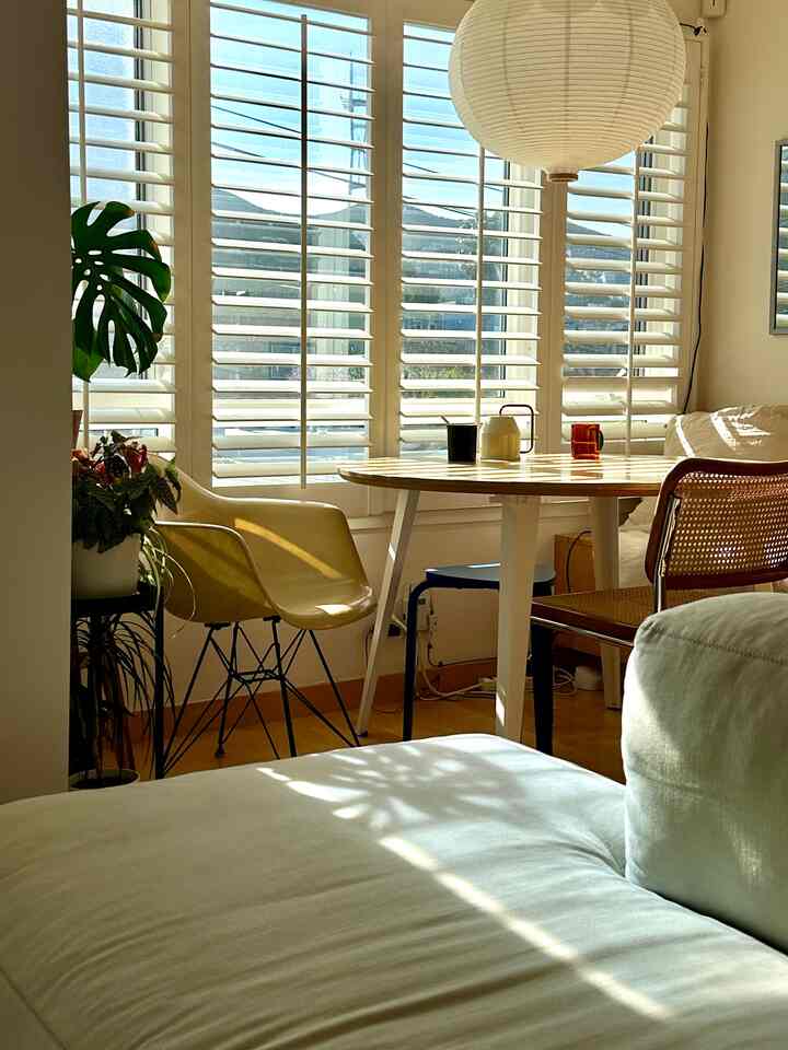 White and yellow toned living-dining room featuring wooden dining table and sofa with cozy sunlight ambiance