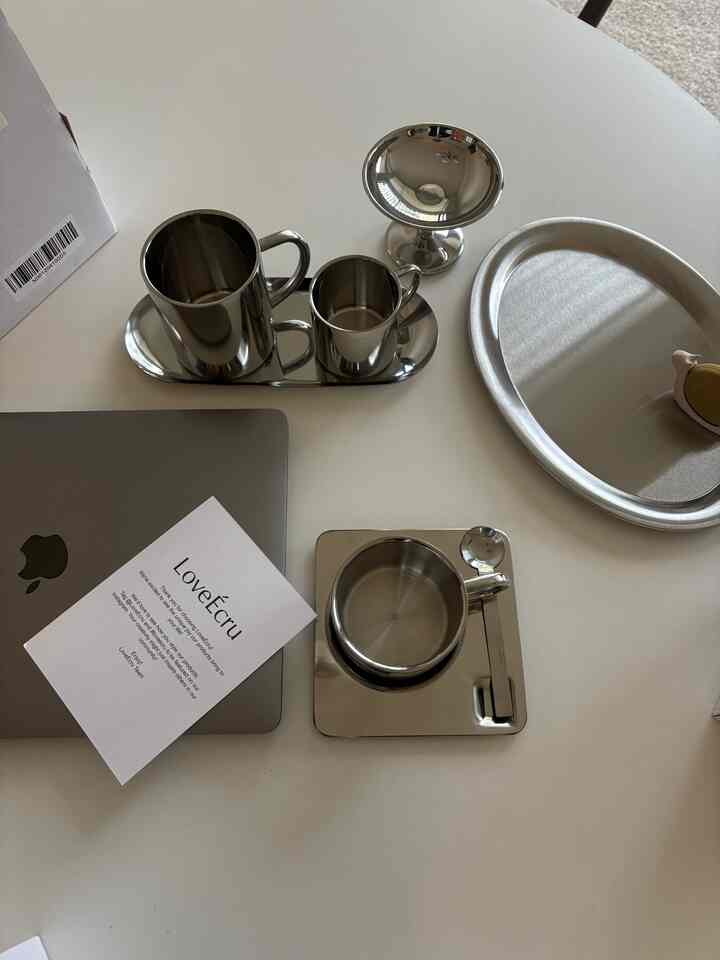 Minimal home cafe table featuring chrome and steel stainless cups, tray, and laptop on a clean surface