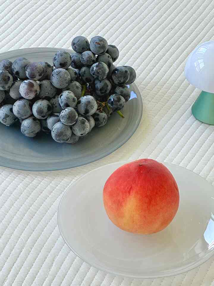 White tablecloth with plates holding peach and grapes, simple summer table setting featuring a mini lamp glow