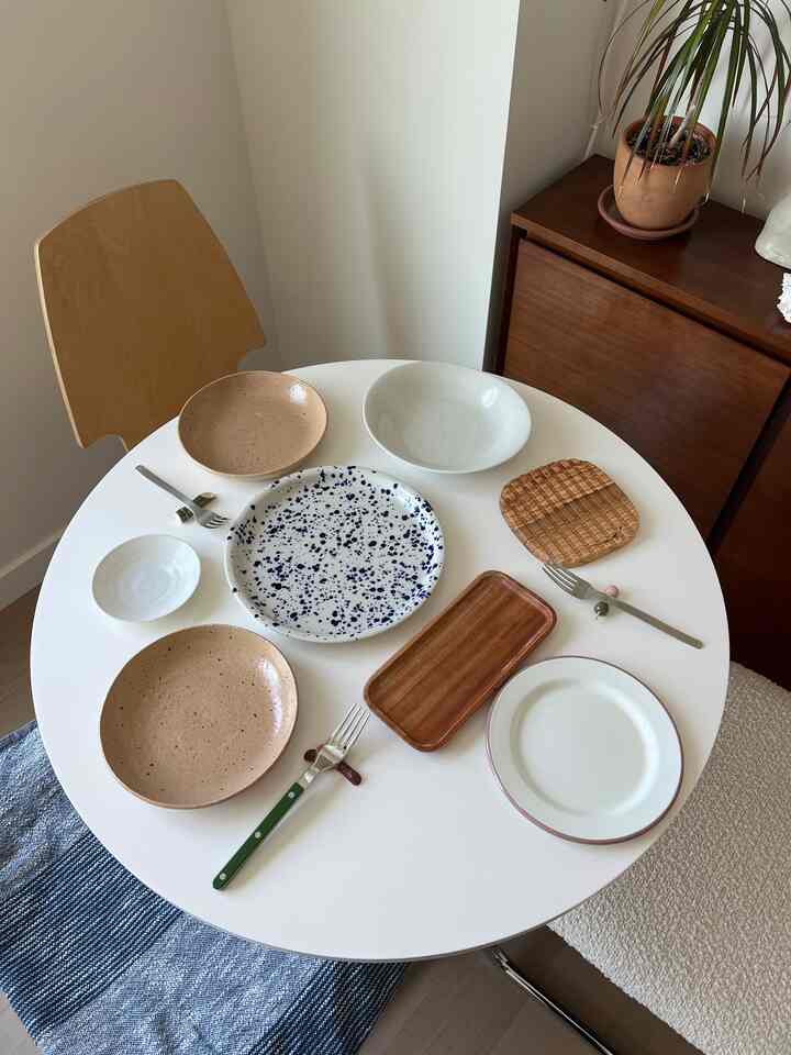 White-toned dining room featuring a round dining table with various plates and a wooden chair, creating a natural atmosphere
