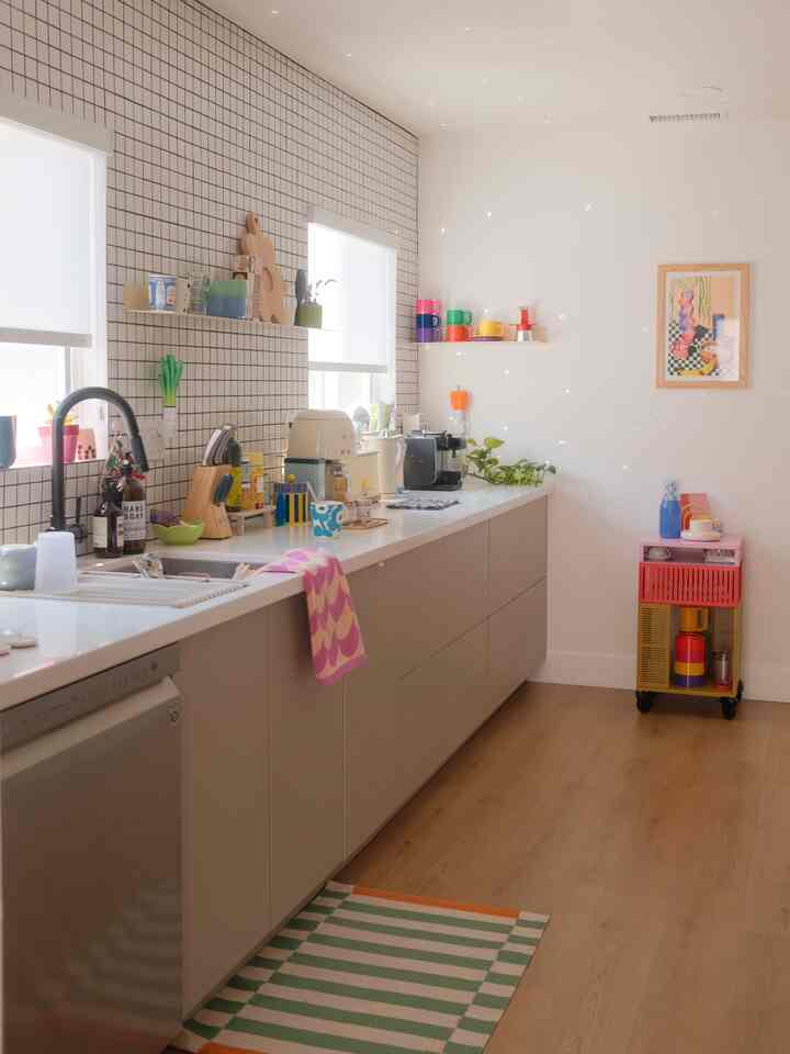 Bright and clean natural-tone kitchen featuring rainbow mugs on shelves and a striped rug adding character