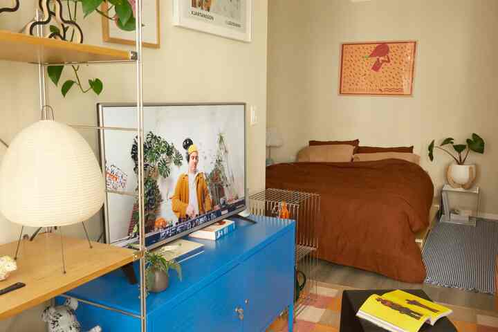 A beige and brown tone bedroom living space featuring a blue TV stand and cozy bedding with a warm atmosphere