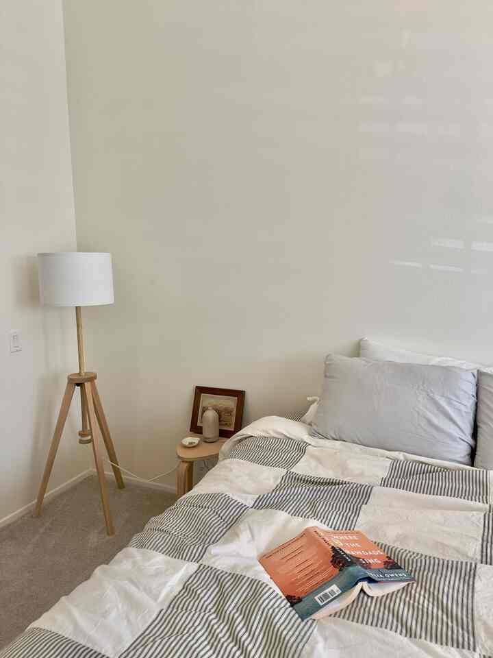 Natural color and white bedroom featuring wooden stool and floor lamp with a cozy atmosphere