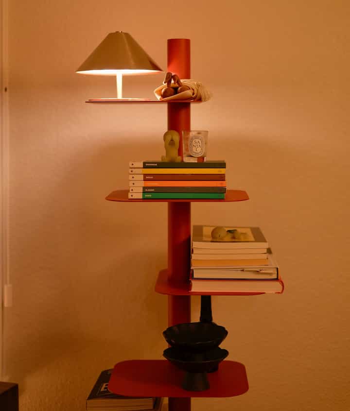 Red-toned living room space featuring a red Story Bookcase with table lamp, candle, and small decorative objects creating a warm atmosphere