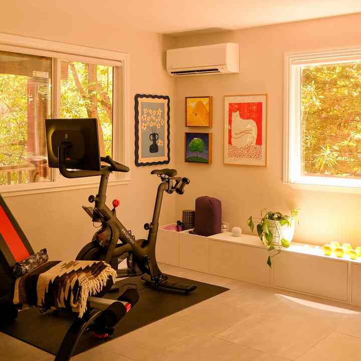 Beige-walled home gym featuring white storage cabinets, a Peloton bike, and yoga accessories in a modern exercise room
