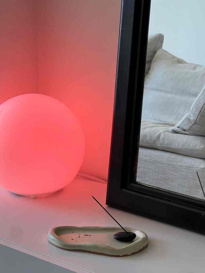 Minimalist small bedroom corner with incense and a pink table lamp on white shelf creating a cozy atmosphere