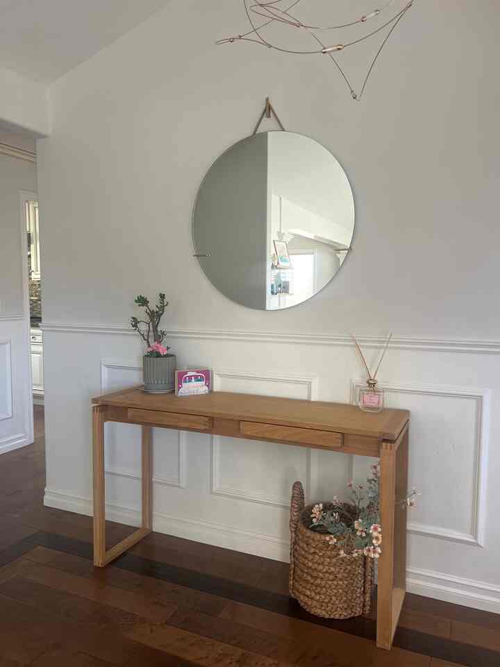 Simple entrance with white walls, wood tone console table, round mirror, and modern chandelier lighting