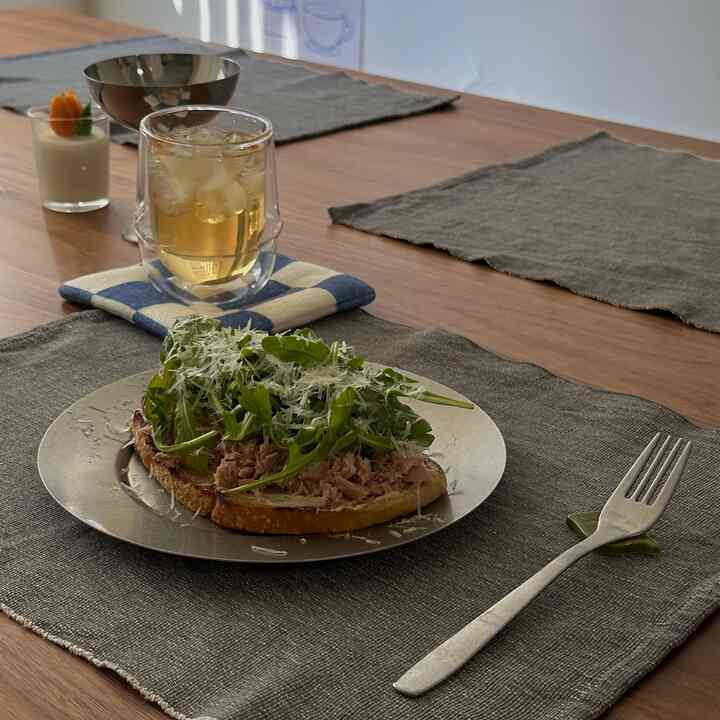 Warm brown wood tone kitchen table with gray linen placemats featuring a fresh brunch plate and iced drink in a cozy setting