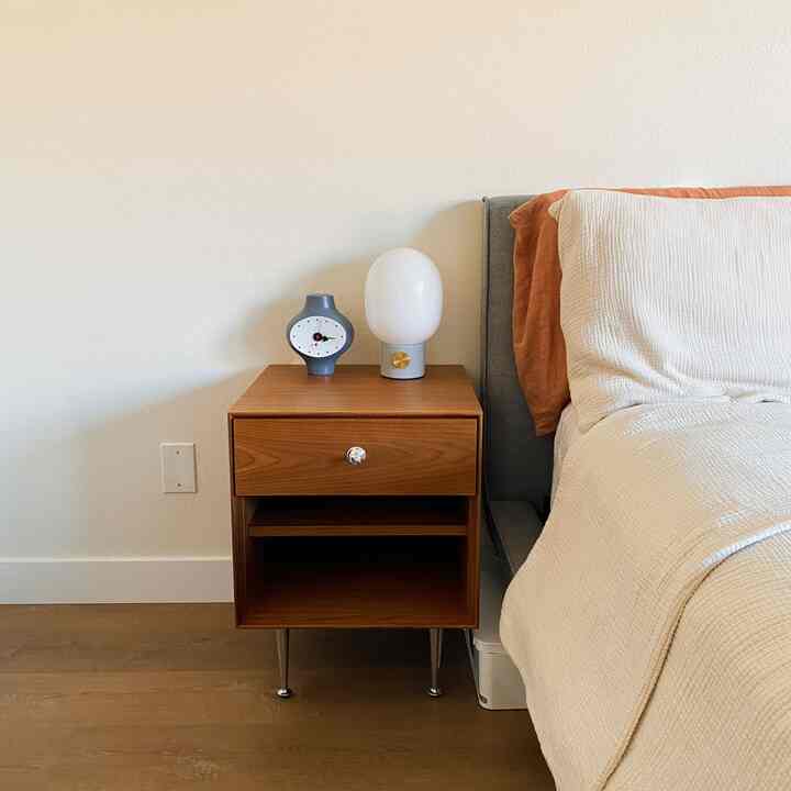 A natural-toned bedroom featuring wood tones, mid-century modern nightstand and table lamp beside a neatly made bed, creating a cozy atmosphere