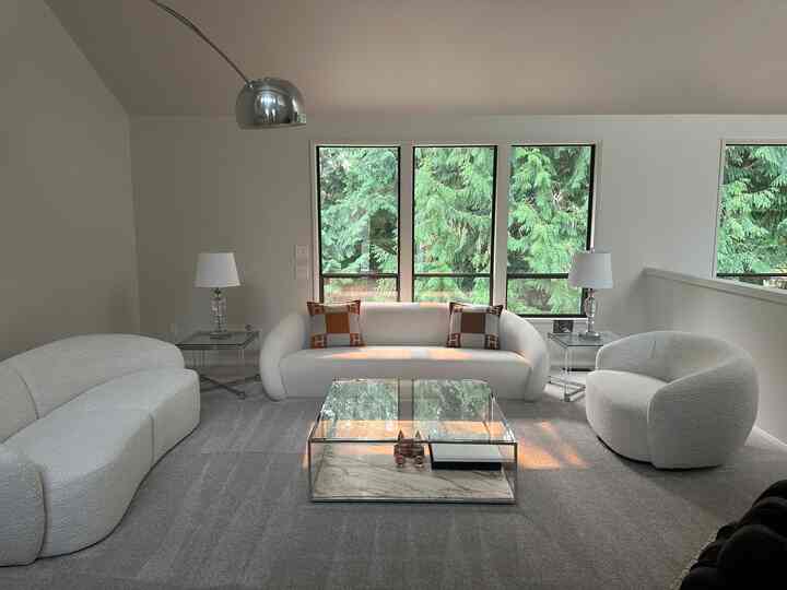A modern living room with white and gray tones, featuring a transparent coffee table centered among sofas and an armchair