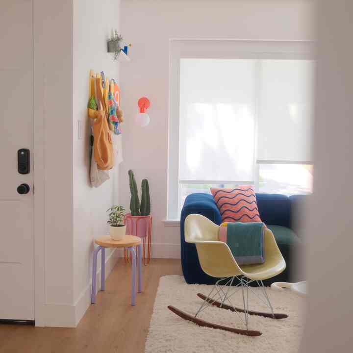 Light-toned entrance corner featuring a yellow rocking chair, blue sofa, and natural wood stool with soft lighting