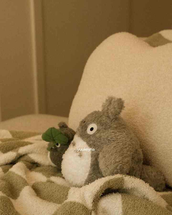 Beige-toned bedroom featuring a bed with Totoro plush doll and checkerboard blanket creating cozy atmosphere