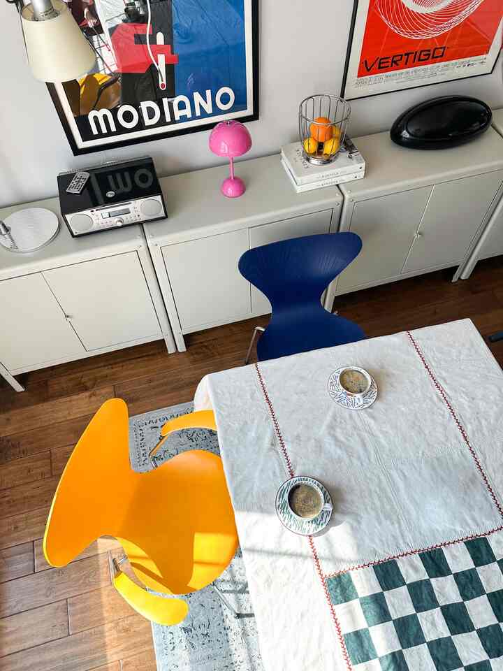 A white and wood-tone dining room featuring a dining table with yellow and blue chairs and coffee cups, creating a cozy home cafe atmosphere