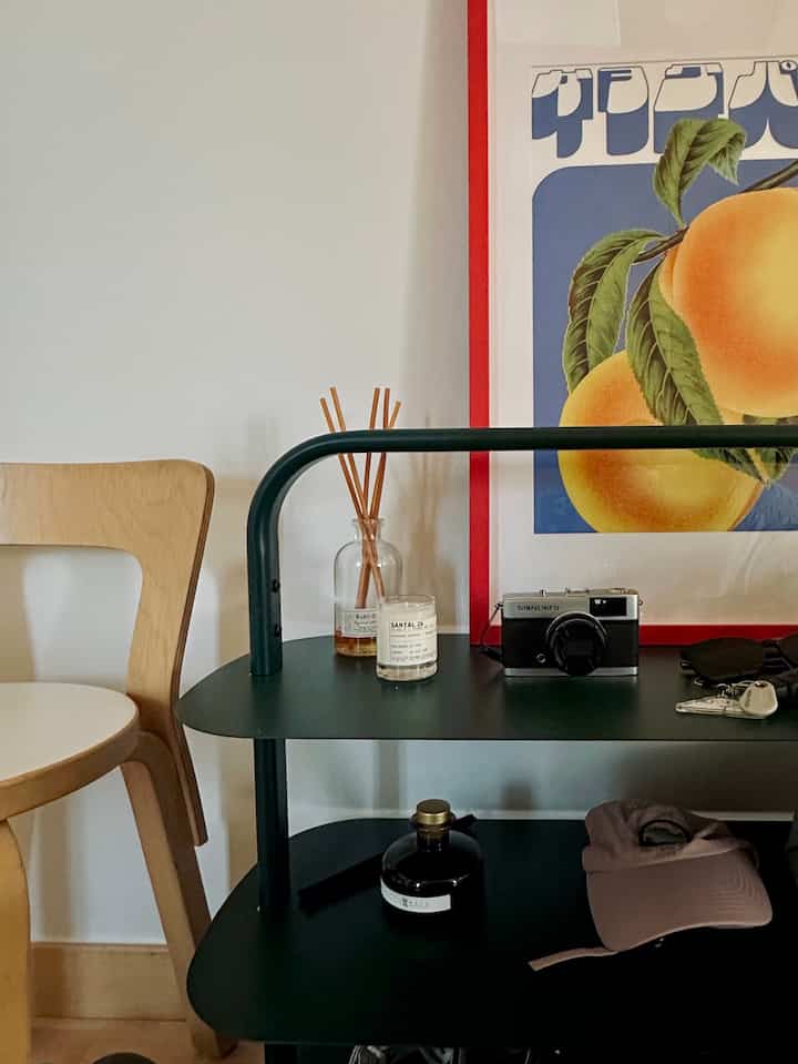 Natural wood tone and dark green shelving in tidy entrance featuring Artek chair, candles, diffuser, and camera accessories