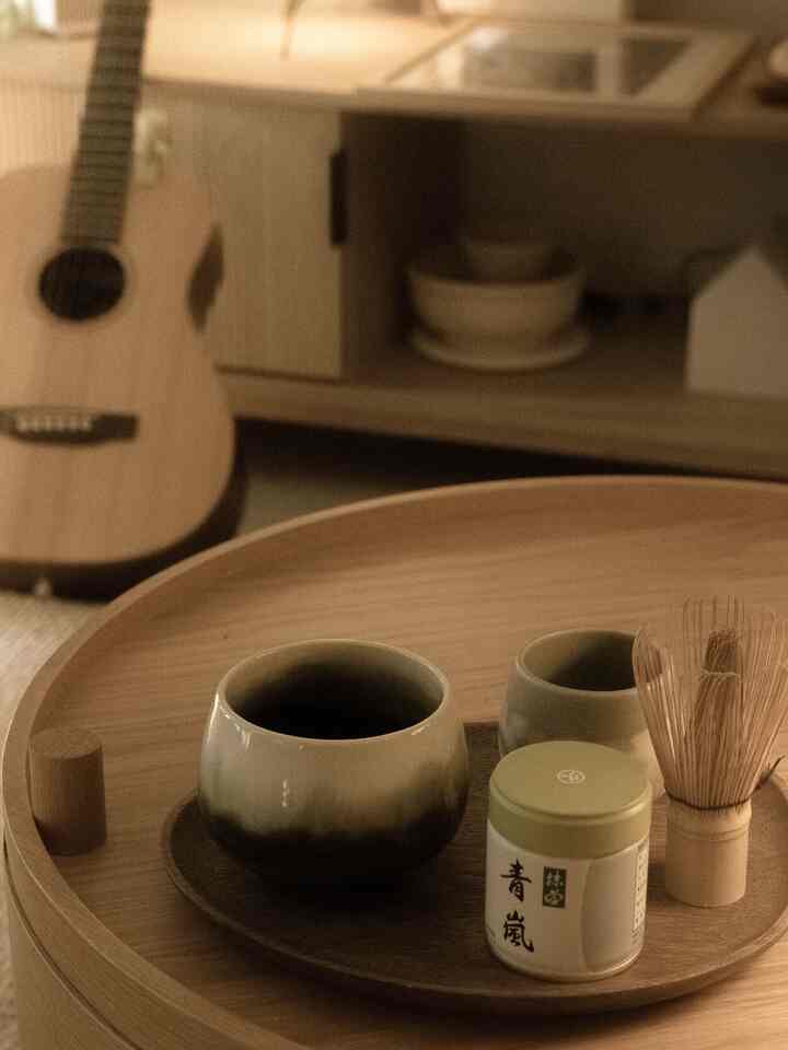 Warm wood-toned living room with Japanese-inspired calm atmosphere featuring a round wooden coffee table holding matcha tools and cups for a cozy home cafe