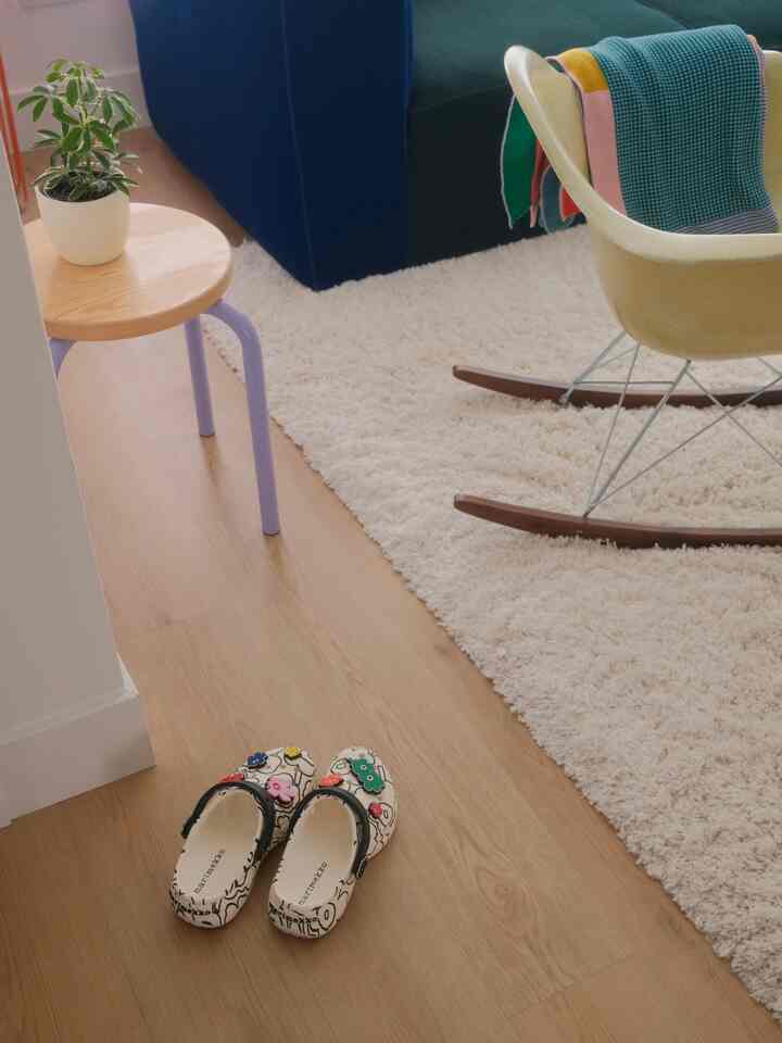 Natural wood tone flooring and cream rug in an entrance featuring a yellow armchair and a plant for a warm atmosphere