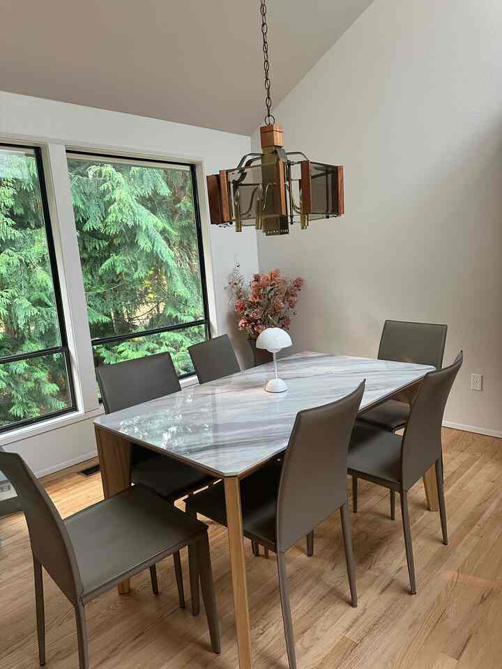 Natural-toned 6-seat dining room with white walls, featuring a marble dining table, white table lamp, and wooden pendant light creating calm ambiance