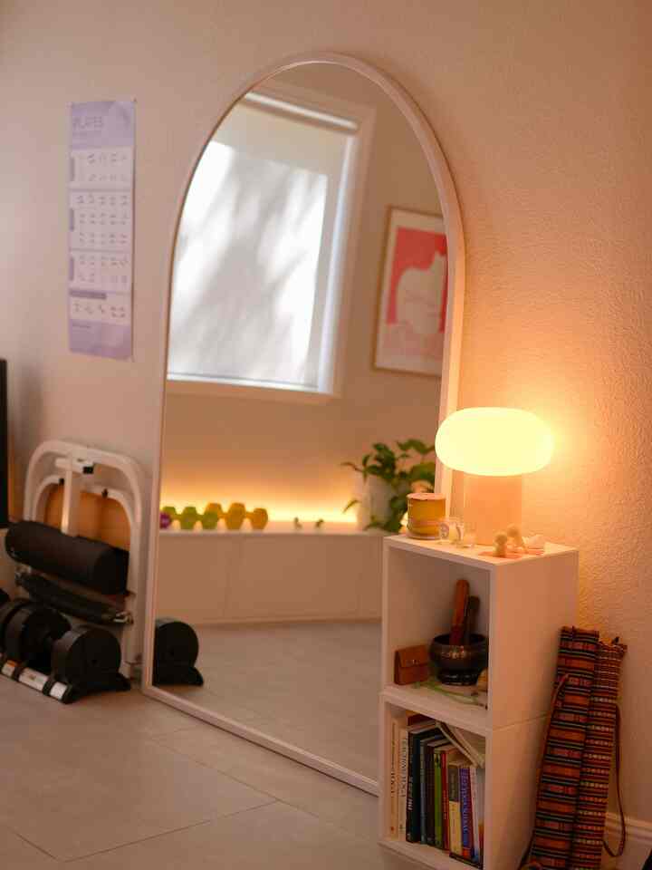 Cozy home gym space with warm beige walls, a full-length arched mirror, and a table lamp