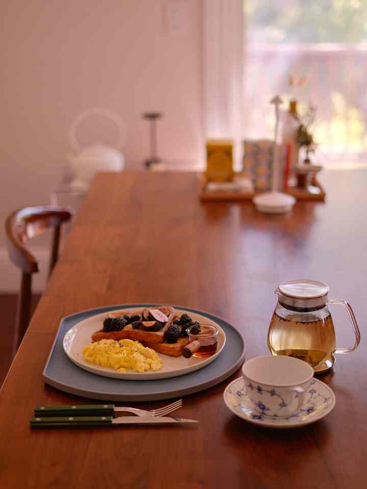 Warm wood tone dining room featuring breakfast plate, cutlery, and tea set evoking cozy home cafe atmosphere
