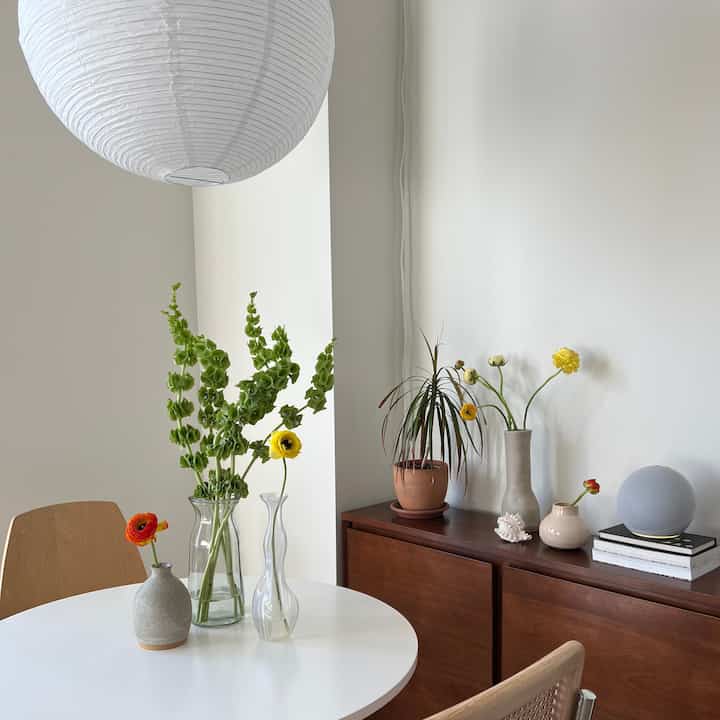 Minimal white-toned dining room featuring wood furniture and vases with natural, calming atmosphere