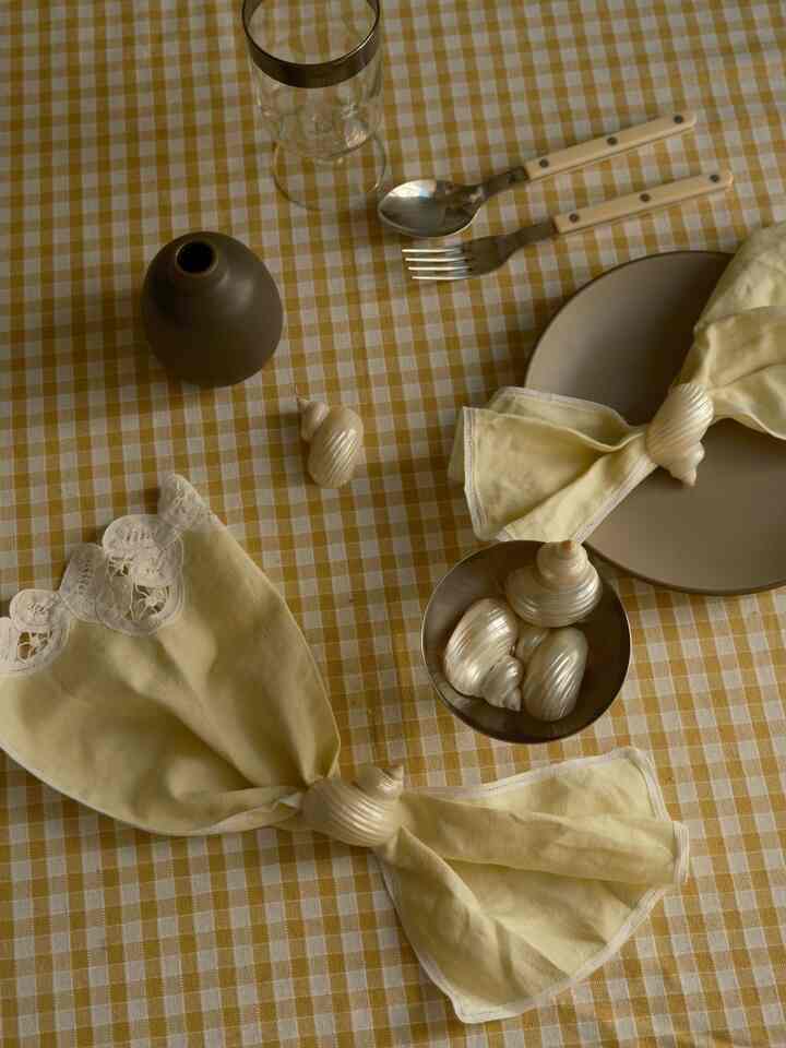 Warm yellow gingham tablecloth dining table featuring vintage seashell napkin rings and cream napkins for an elegant vibe