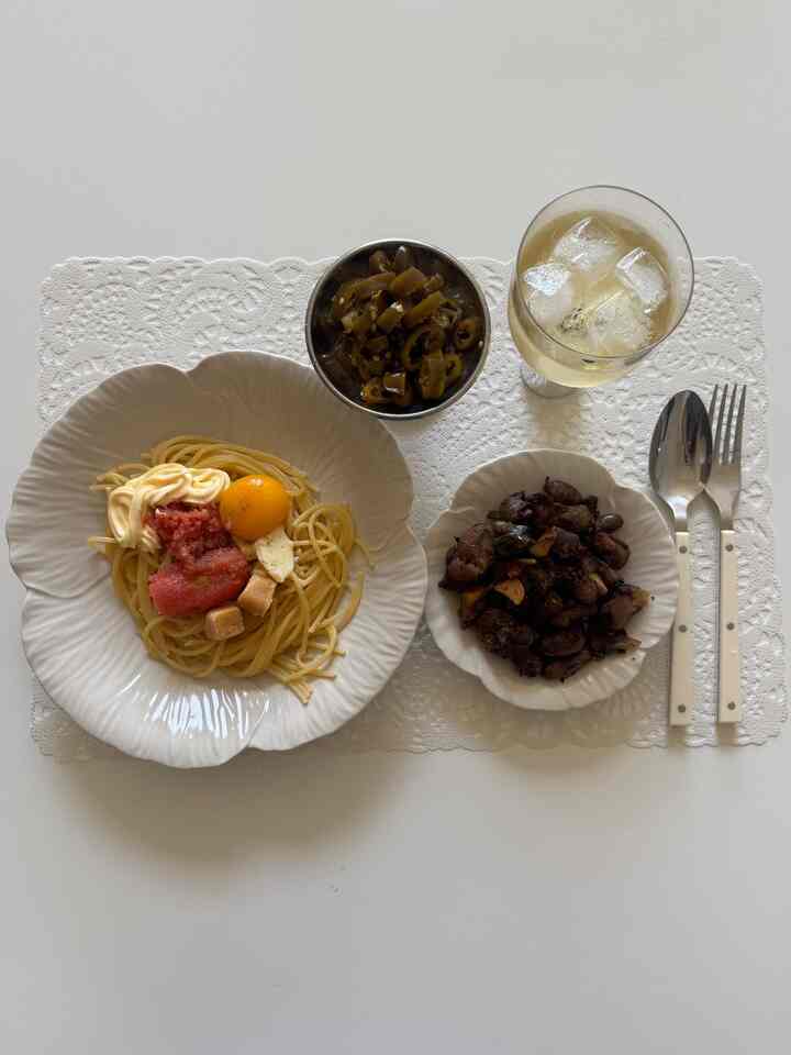 White dining table featuring white plates and bowls with mentaiko pasta and side dishes, presenting a clean and simple meal setting