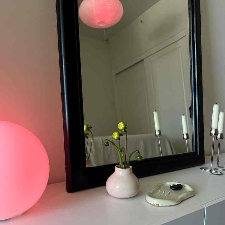 White-toned bedroom featuring a black-framed mirror, vase with flower buds, and a candlestick creating a minimal atmosphere