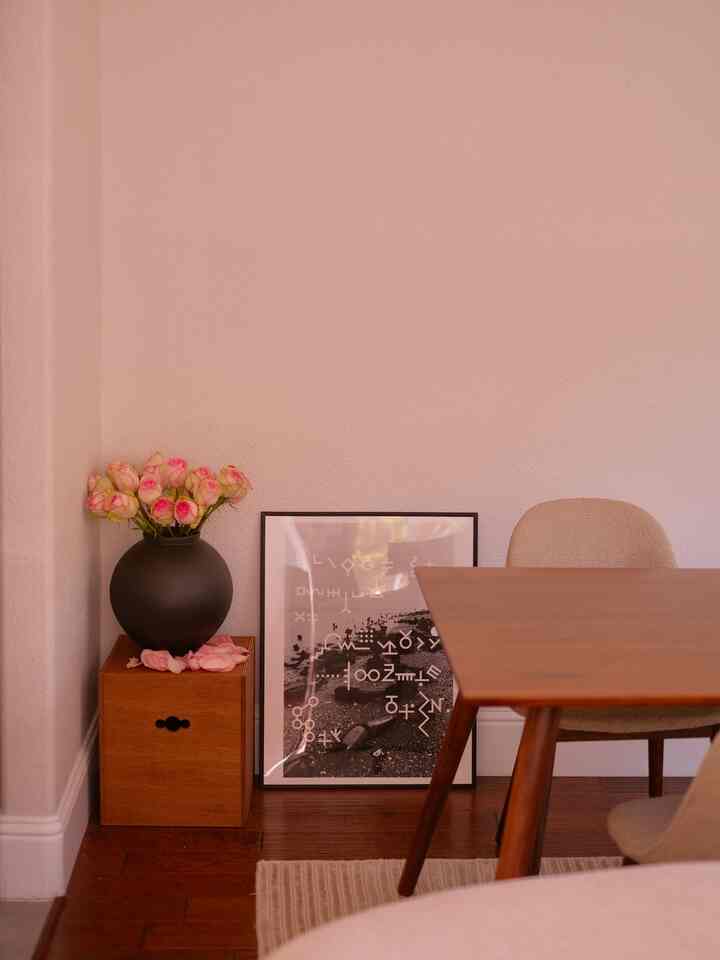 Natural dining room in brown wood tone and beige colors featuring a dining table, vase with flowers, and a poster with warm atmosphere