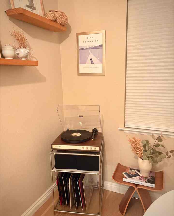 Warm beige corner space with wood tone furniture featuring a Crosley turntable, framed picture, and stool creating a cozy retro atmosphere
