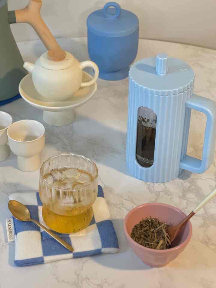 Natural beige and soft blue toned home cafe table featuring teapot, glass with iced tea, and a coaster creating a cozy autumn atmosphere