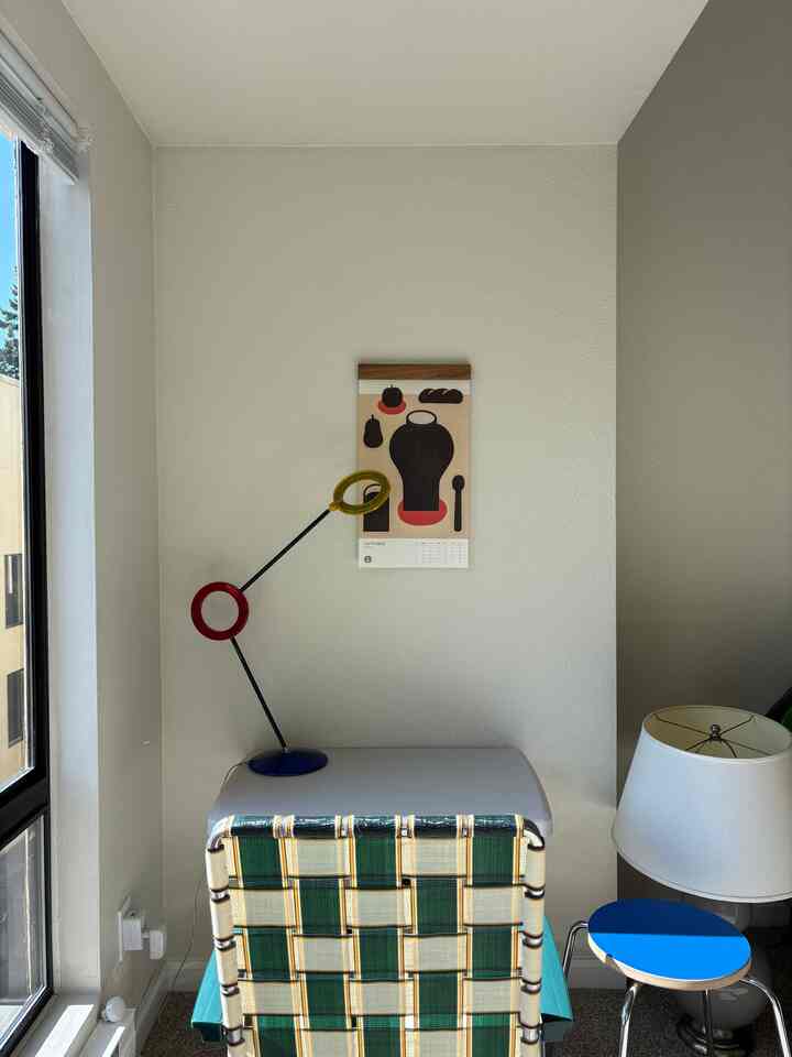 Home office corner with white walls and natural light, featuring a desk and a green checkered chair with colorful table lamp