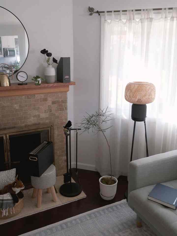 Bright white and brown toned living room corner featuring sofa, floor lamp, plants, and fireplace with natural modern style