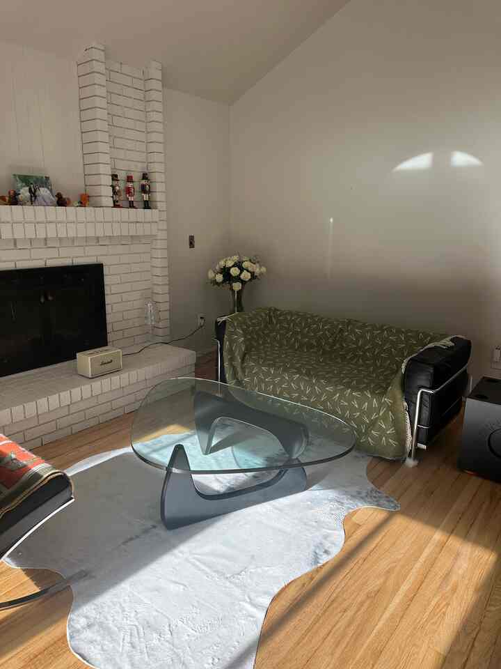 Living room with white walls and fireplace, black sofa draped with olive blanket, and glass coffee table creating a warm atmosphere