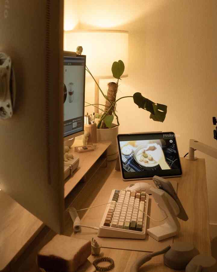 Warm wood tones and white accents define this home office featuring a desk with monitor, keyboard, plant, and table lamp in a cozy workspace