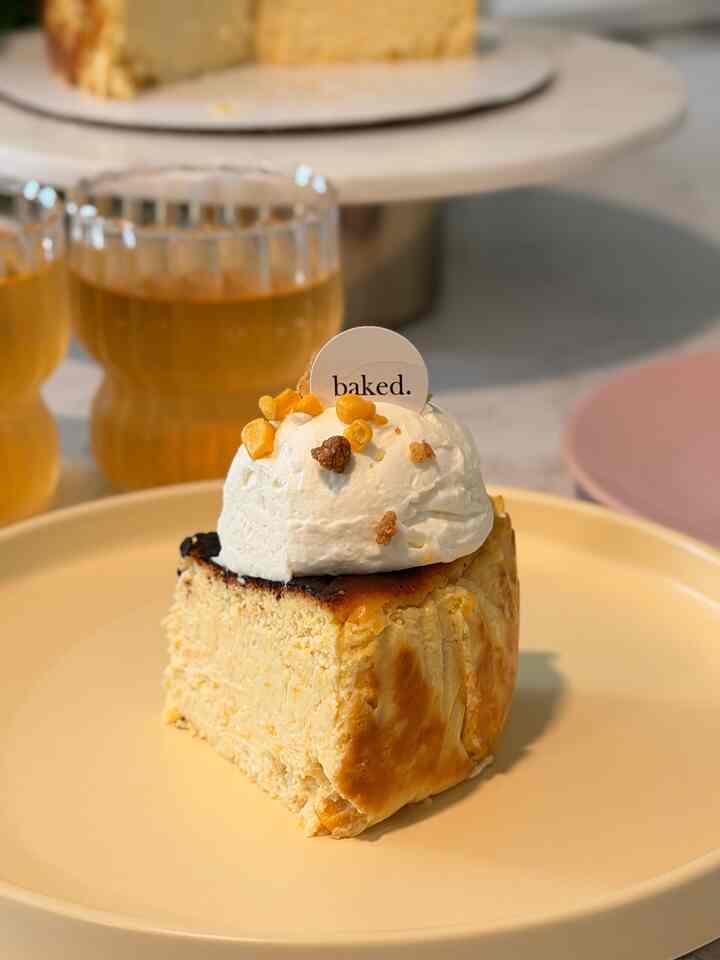 Warm gold-toned home cafe setup featuring a Basque cheesecake slice with whipped cream on a gold plate