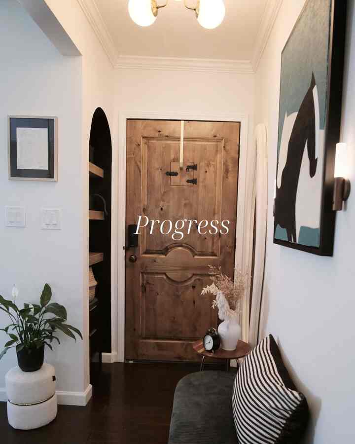 Cozy entrance featuring a wood tone door and white walls, accented with a sofa, stool, and wall sconce lighting